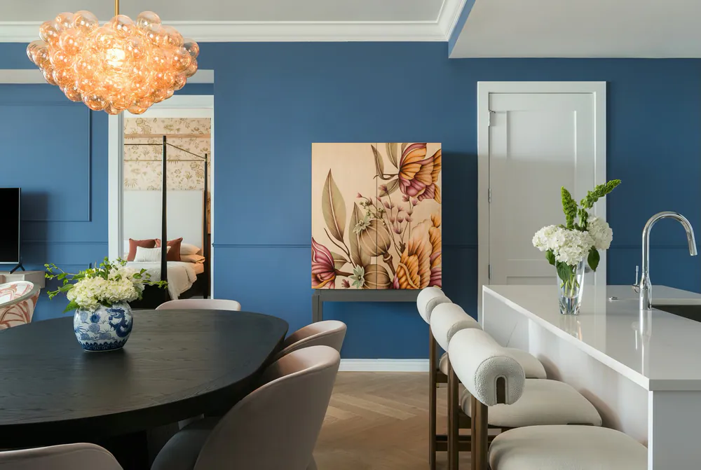 Dining area with blue walls, amber glass bubble chandelier, black table, blush chairs and bouclé stools at a white island, at Art House in Downtown St. Petersburg. Interior design by MJ Designs