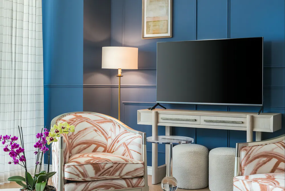 Sitting area with blue paneled walls, brass floor lamp, pale oak console, bouclé poufs and coral patterned armchairs, at Art House in Downtown St. Petersburg. Interior design by MJ Designs
