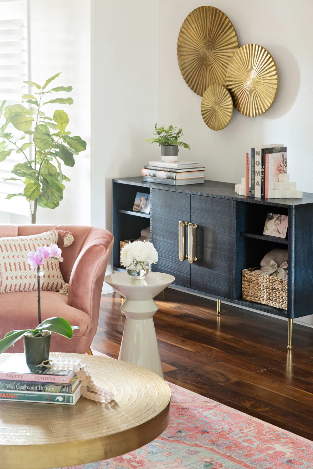 Black credenza with brass pulls, fiddle leaf fig and blush velvet chair beside plantation shutters, at Bayou Grande in St. Petersburg. Interior design by MJ Designs