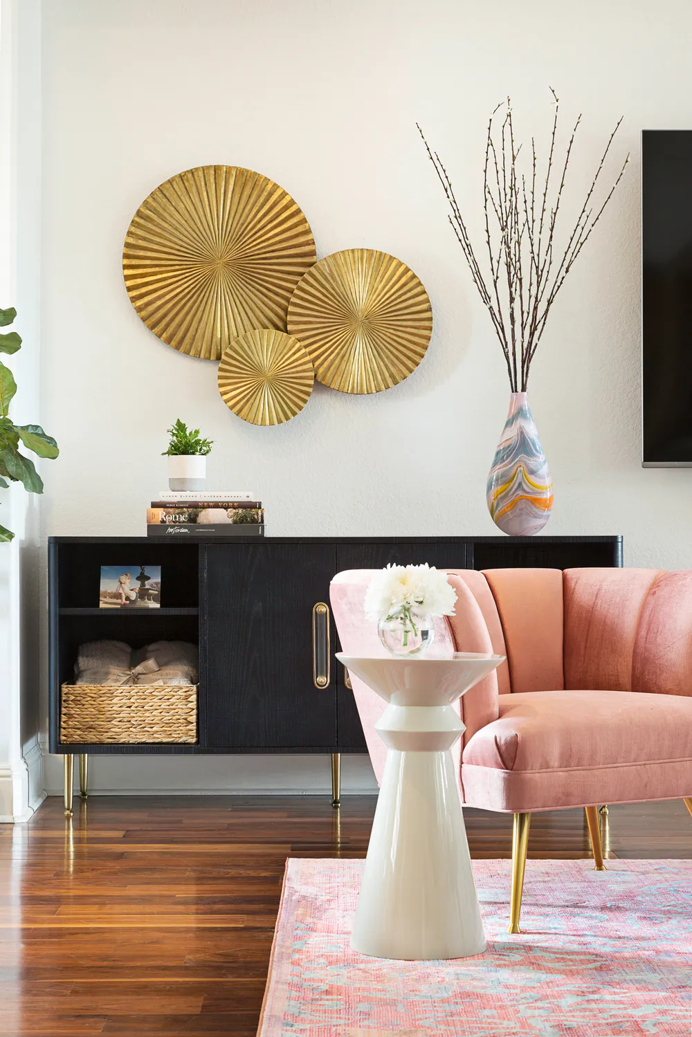 Black credenza with brass sunburst discs, marbled glass vase and blush velvet chair, at Bayou Grande in St. Petersburg. Interior design by MJ Designs