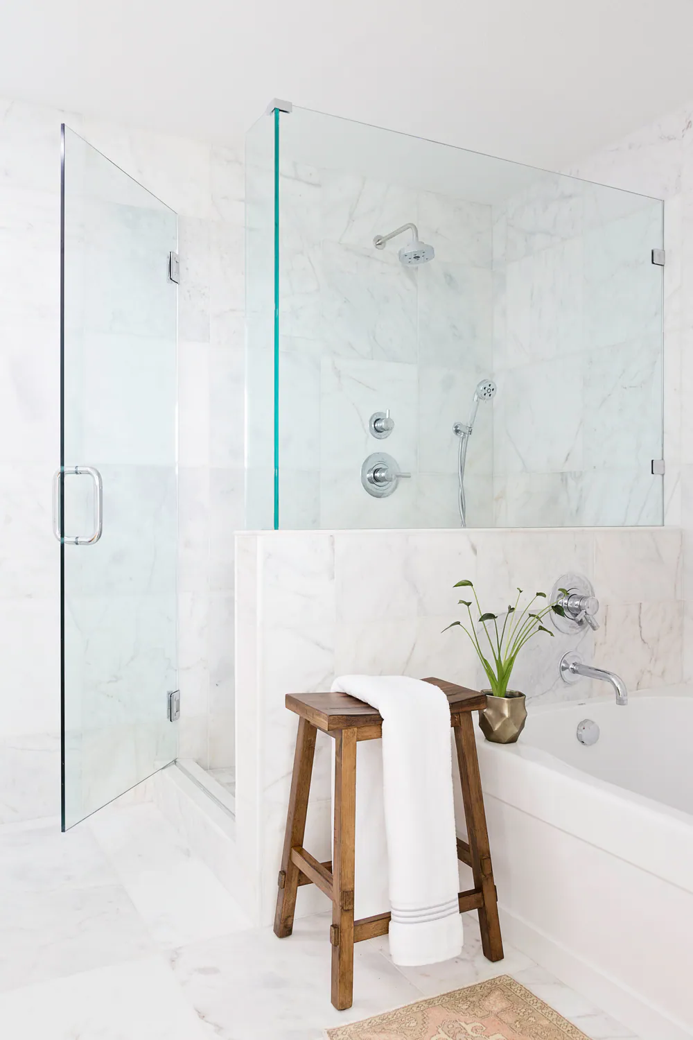 Marble walk-in shower and soaking tub with a wooden stool and white towel, at Bayshore in Tampa. Interior design by MJ Designs