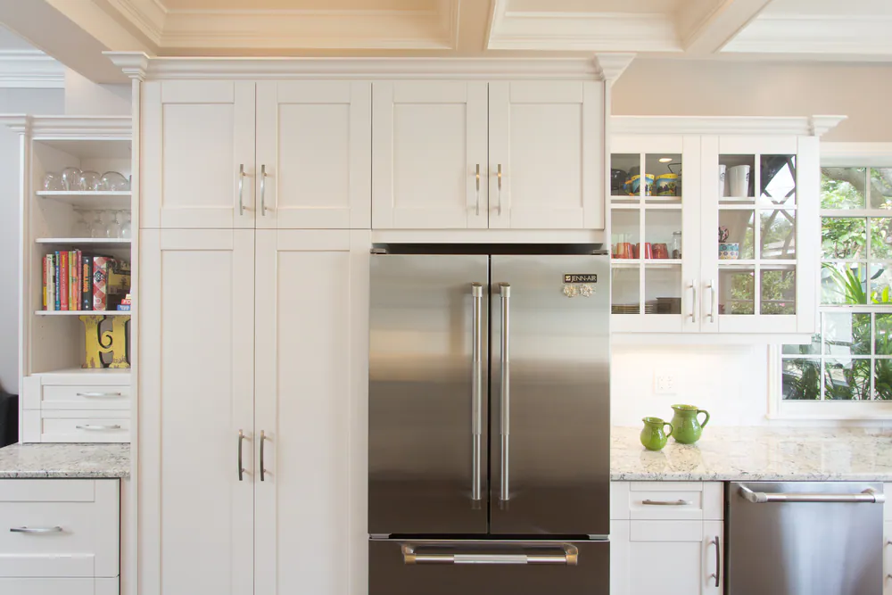 White shaker cabinetry framing a stainless French door refrigerator, with open shelves and glass-front uppers, at Brightwaters in St. Petersburg. Interior design by MJ Designs