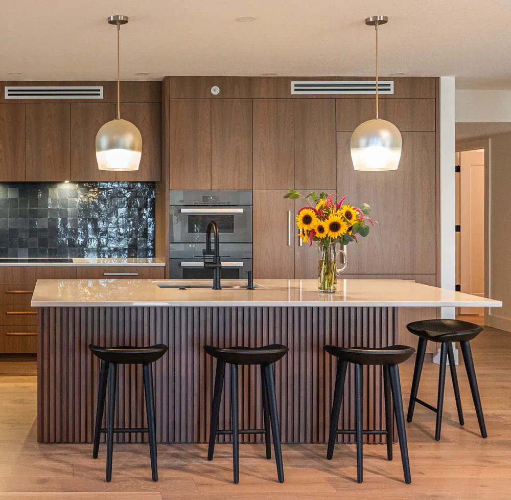 Kitchen with walnut cabinetry, reeded walnut island, glossy charcoal tile and black saddle stools, at Downtown St. Pete Condo in St. Petersburg. Interior design by MJ Designs