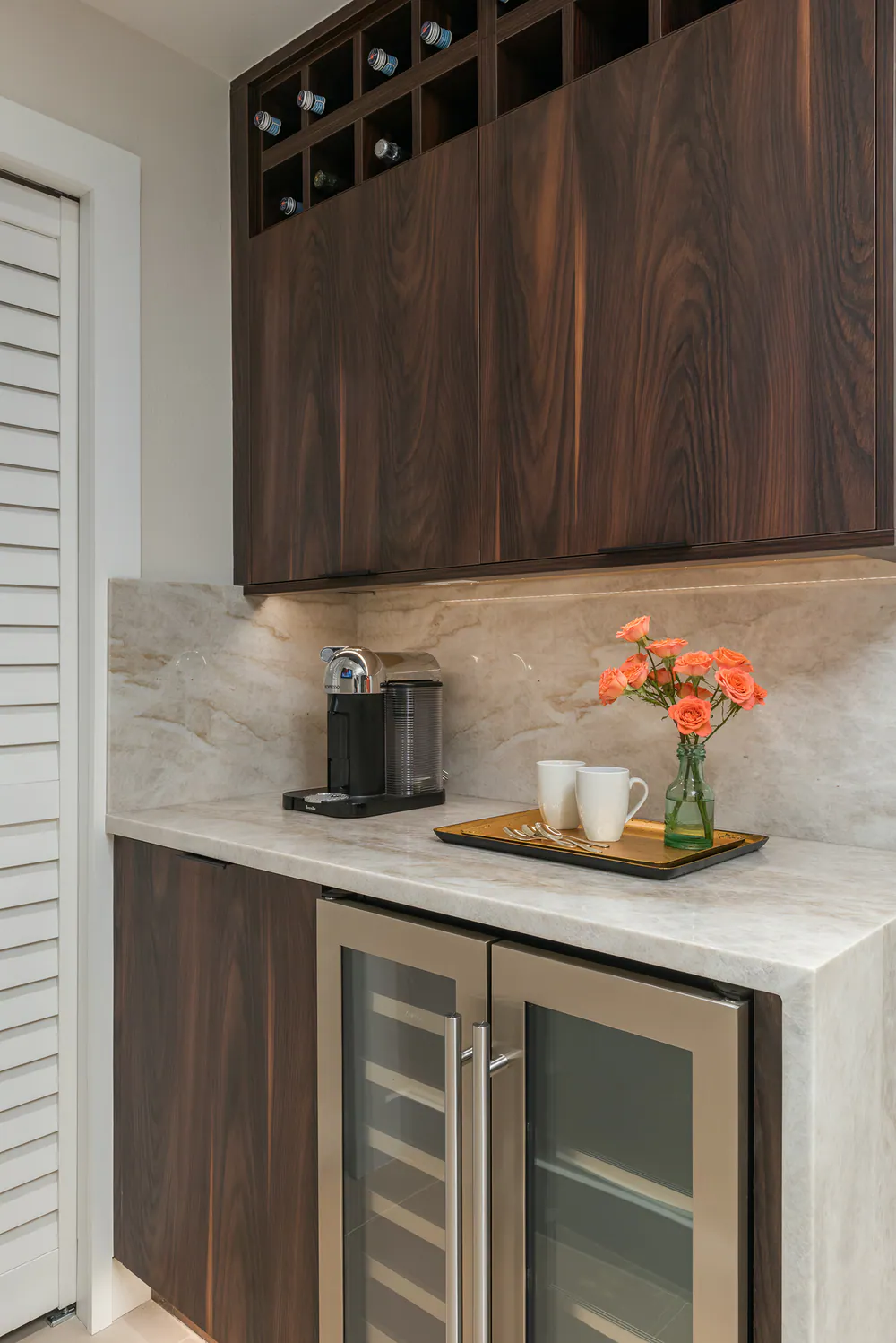 Coffee bar with wine cubbies, veined stone backsplash and glass-front beverage fridge, at Gulf Beaches Condo in Pinellas County. Interior design by MJ Designs