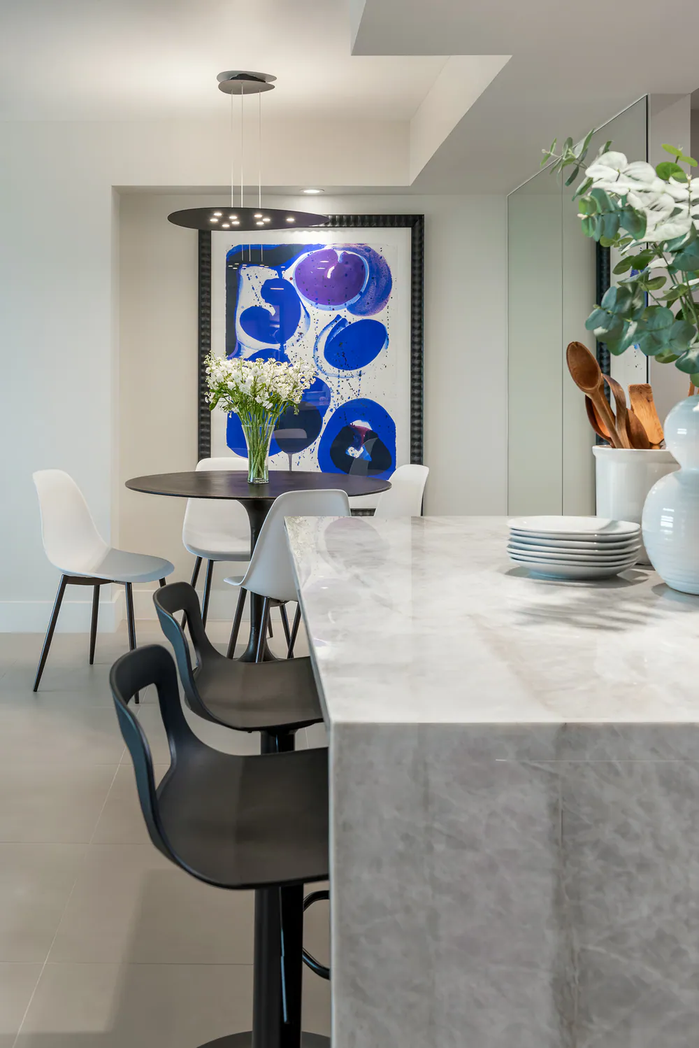 Stone island with black counter stools and a round black dining table beyond, at Gulf Beaches Condo in Pinellas County. Interior design by MJ Designs