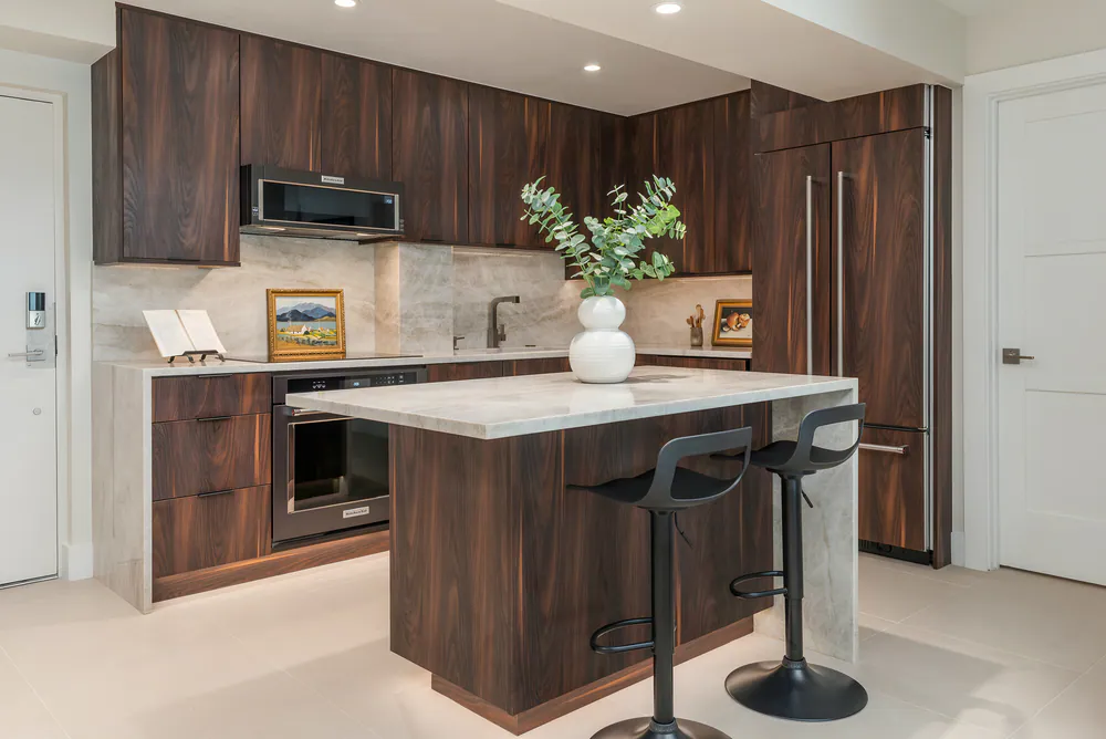 Kitchen with island, waterfall stone top and two black counter stools, at Gulf Beaches Condo in Pinellas County. Interior design by MJ Designs