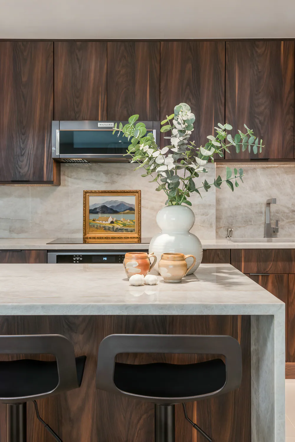 Kitchen island with waterfall stone top, black stools, eucalyptus and pottery, at Gulf Beaches Condo in Pinellas County. Interior design by MJ Designs