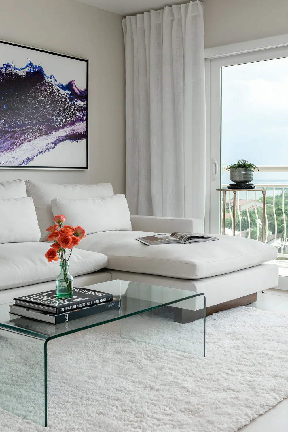 White chaise sectional beside sheer linen drapery and a balcony door with water view, at Gulf Beaches Condo in Pinellas County. Interior design by MJ Designs