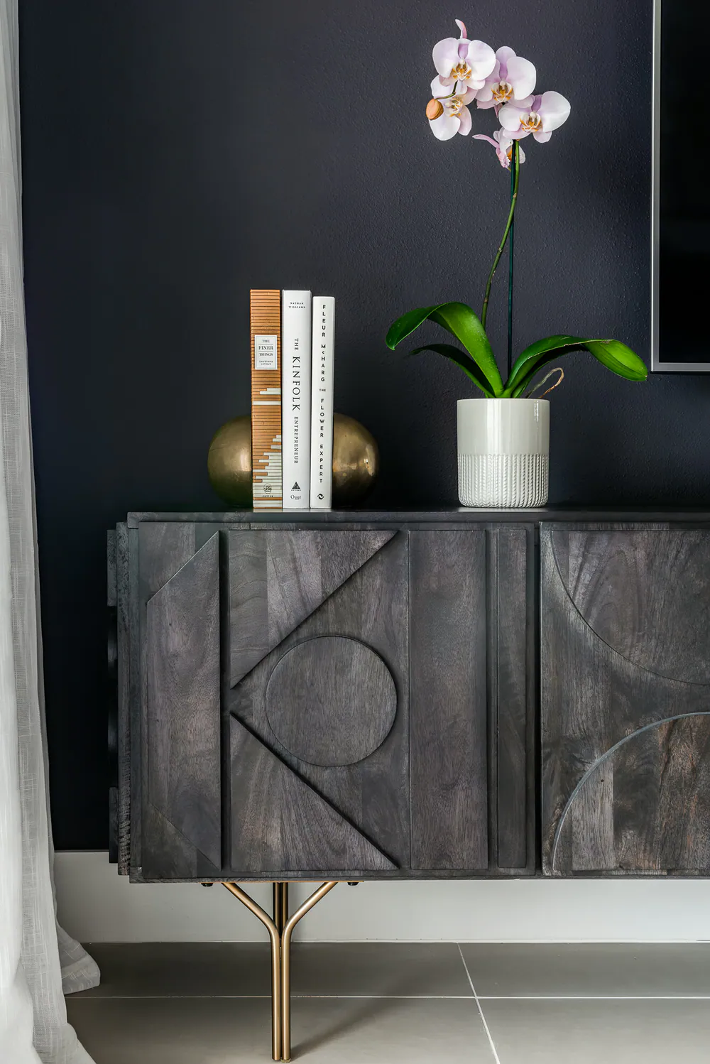 Carved charcoal wood console on brass legs against a deep navy wall, orchid and books, at Gulf Beaches Condo in Pinellas County. Interior design by MJ Designs