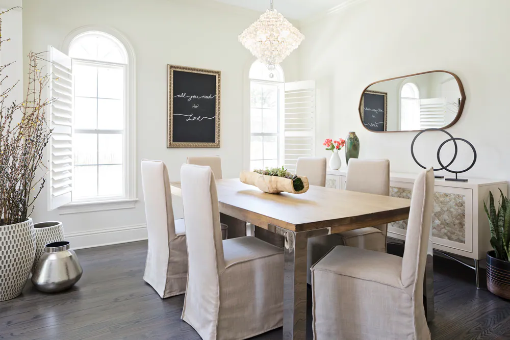 Dining room with wood and polished steel table, slipcovered chairs, crystal chandelier and shell-fronted sideboard, at Hyde Park in Tampa. Interior design by MJ Designs