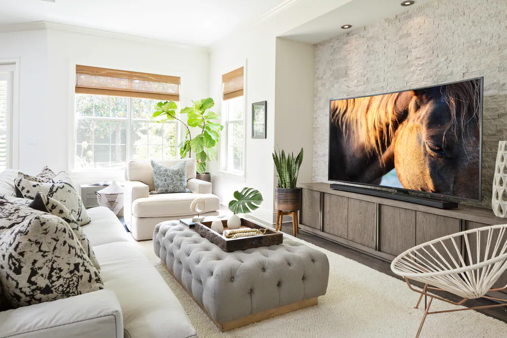 Family room with stacked stone media wall, tufted ottoman and linen seating, at Hyde Park in Tampa. Interior design by MJ Designs