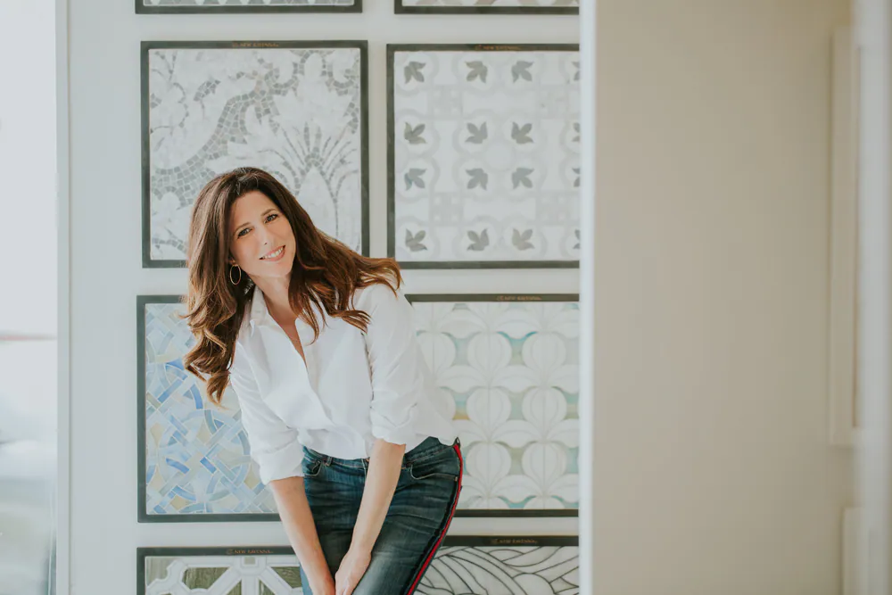 Michelle Jennings, owner and principal interior designer of MJ Designs, in front of a wall of marble mosaic tile samples
