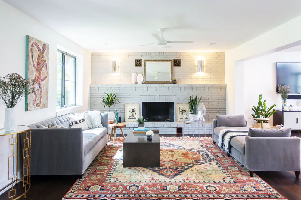 Living room with a white painted brick fireplace, gray velvet sofas and a red and navy Persian rug, at Parkland Estates in Tampa. Interior design by MJ Designs