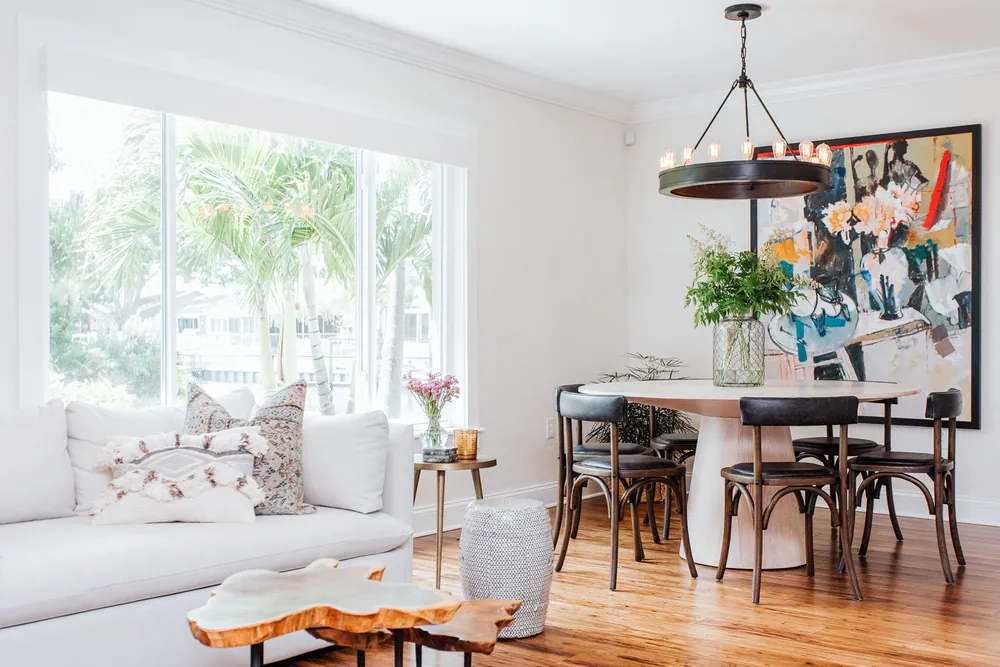 Living and dining room with a white sofa, live-edge coffee table and round pedestal table beneath an iron ring chandelier, at Shore Acres in St. Petersburg. Interior design by MJ Designs