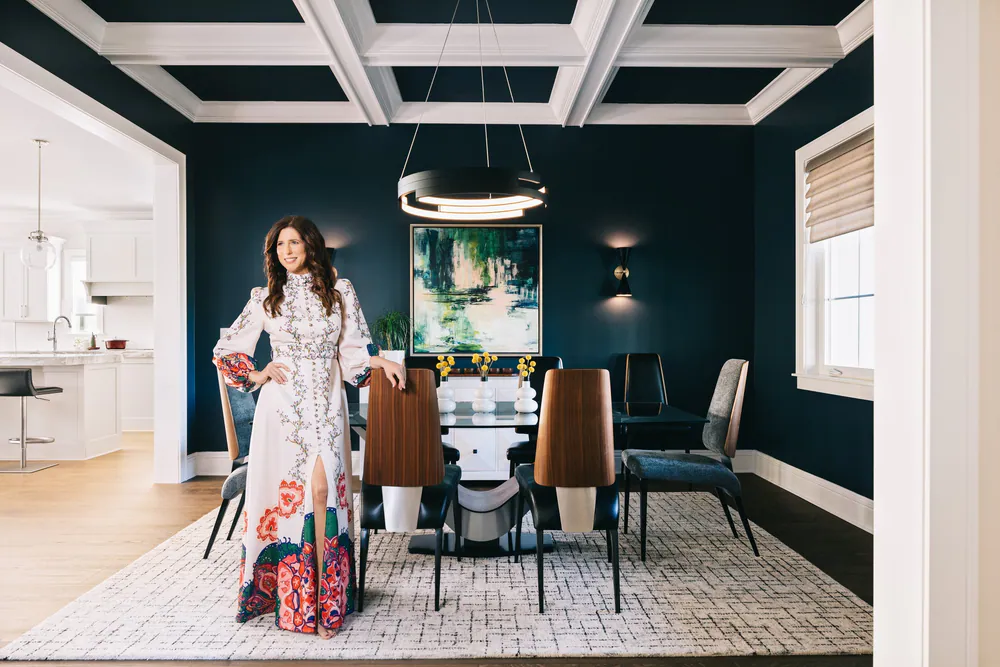 Navy dining room with a white coffered ceiling, ring chandelier and abstract painting, Michelle Jennings standing by the table, at Snell Isle in St. Petersburg. Interior design by MJ Designs